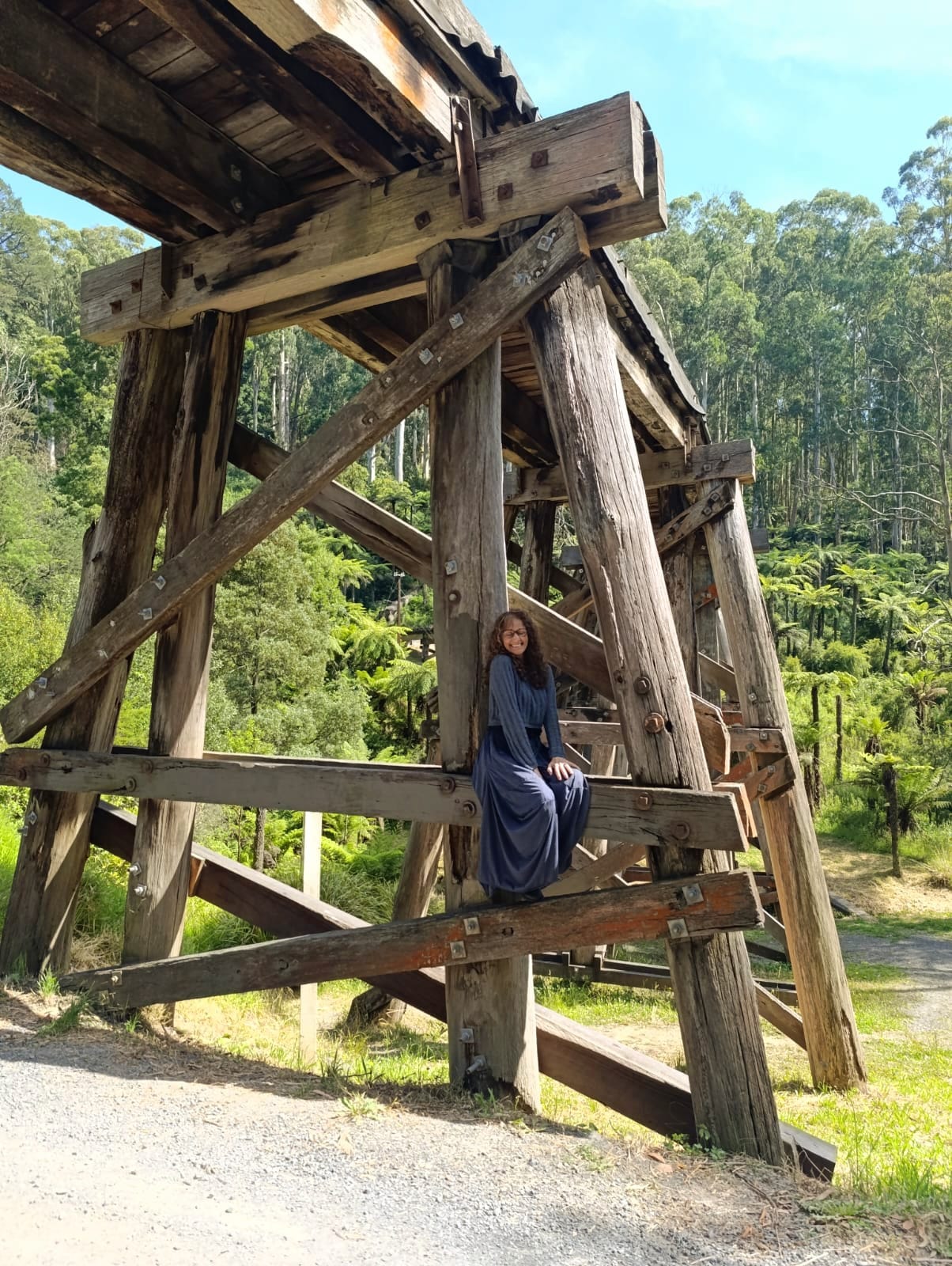 Martina Patania sitting on the timber trestle bridge surrounded by ferns and forest